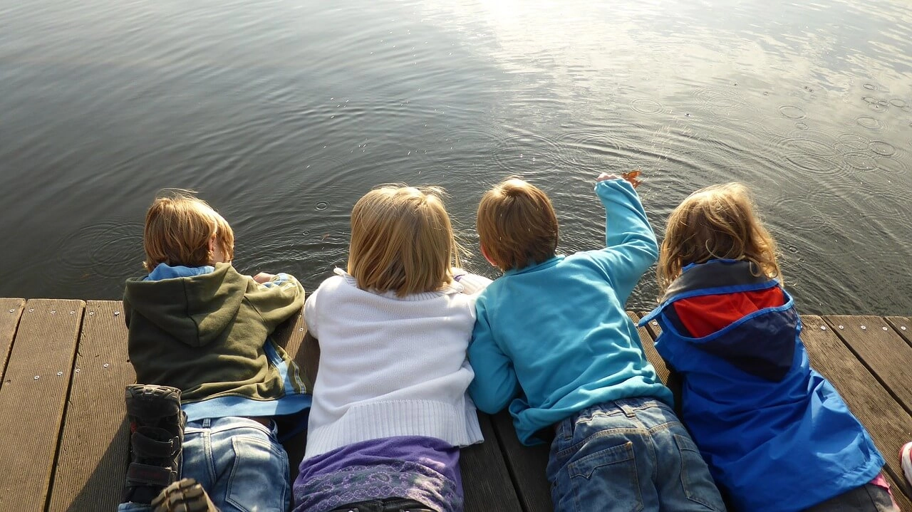 top view of children on a wooden deck looking down at the water of a lake