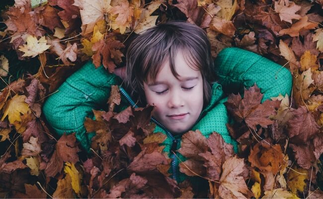 child lying down and buried by leaves