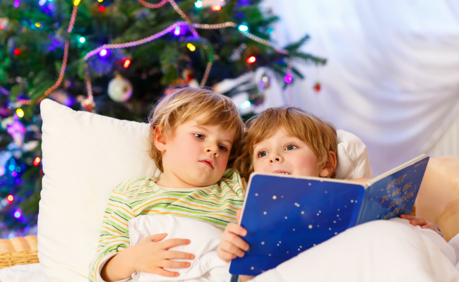 2 children reading a book by a Christmas tree