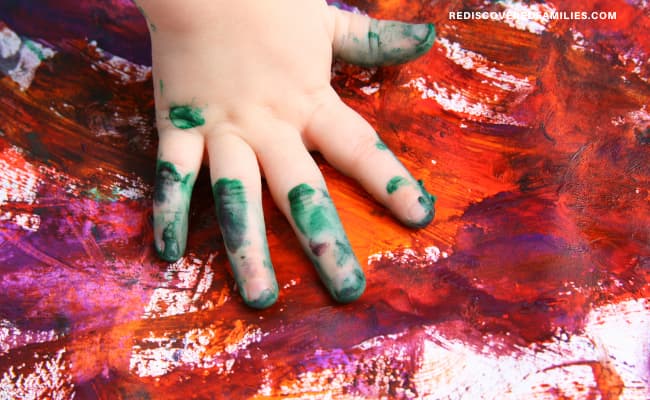 child's hand finger moving paint over the paper