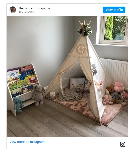 teepee with a rug and cushions next to some canvas shelves full of books