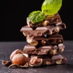 a stack of hazelnut chocolate bark displayed with hazelnuts and a mint leaf.