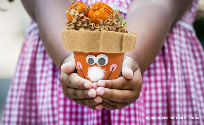 childs hands holding a finished clay pot pumpkin pie craft