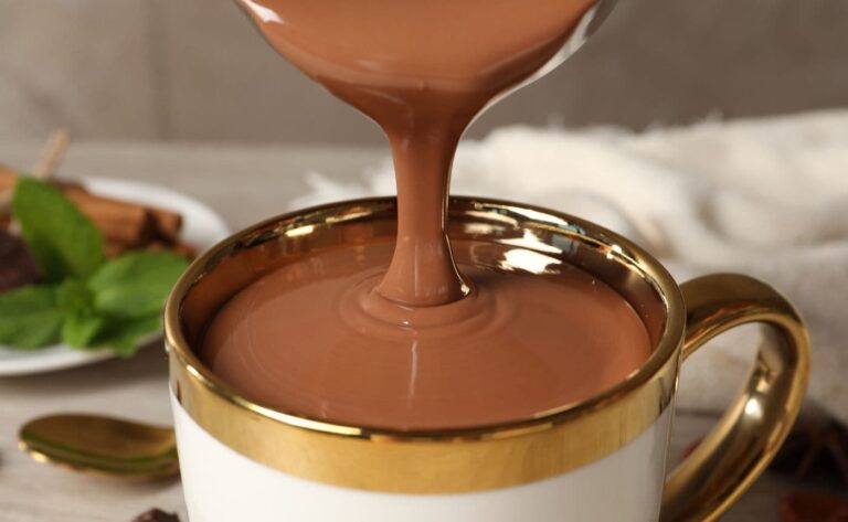 A close-up of thick, creamy Italian hot chocolate being poured into a white and gold mug