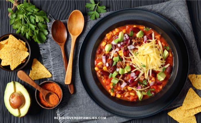 A beautifully styled bowl of taco soup surrounded by fresh herbs, tortilla chips, and wooden spoons.