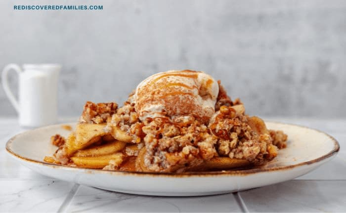 A plated serving of warm apple crisp topped with vanilla ice cream and drizzled with caramel.
