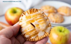 A hand holding a golden apple hand pie with a sweet glaze drizzled on top.