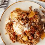 A plate of warm apple crisp topped with vanilla ice cream and drizzled with caramel sauce.