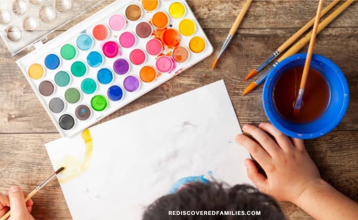 child with paints and a blank piece of paper