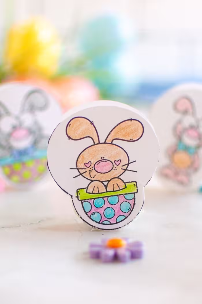 A pin with a wobble bunny craft standing upright with a colorful Easter background