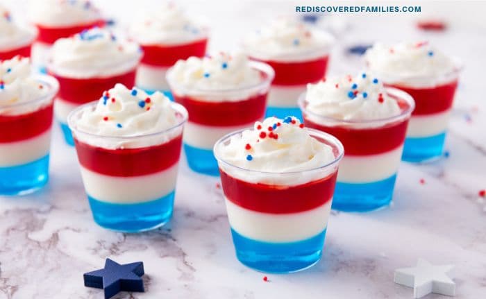 4th of July Jello shots with red, white, and blue layers topped with whipped cream and sprinkles.