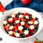 A finished July 4th fruit salad with blueberries, strawberries, and apple stars in a white bowl.