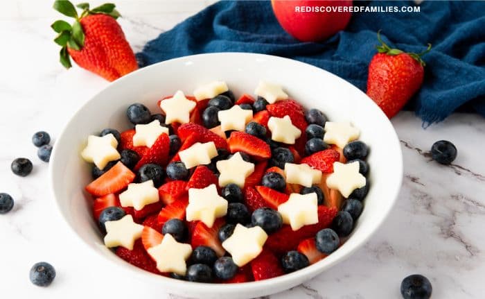 A finished July 4th fruit salad with blueberries, strawberries, and apple stars in a white bowl.