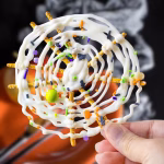Hand holding a completed Halloween chocolate pretzel spider web decorated with festive sprinkles
