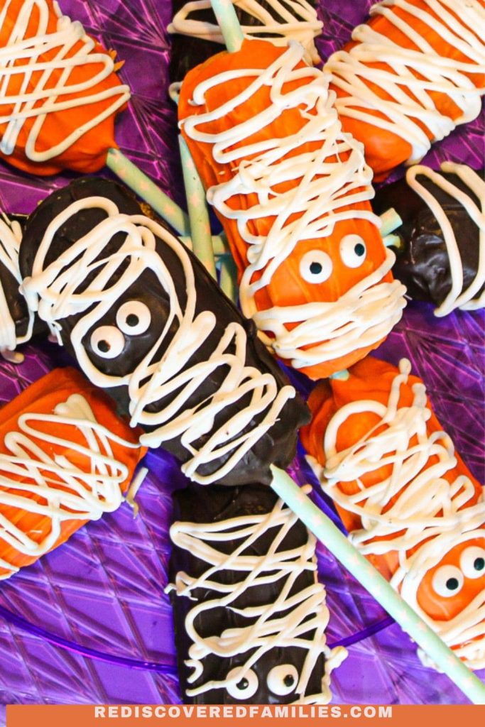Halloween Twinkie mummies, decorated with white candy "bandages" and googly eyes, are displayed on a purple tray.
