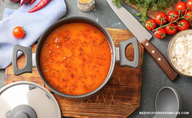a pot of soup on a wooden board surrounded with vegetables