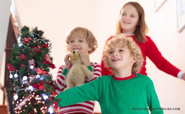 Three smiling children in Christmas pajamas coming down the stairs