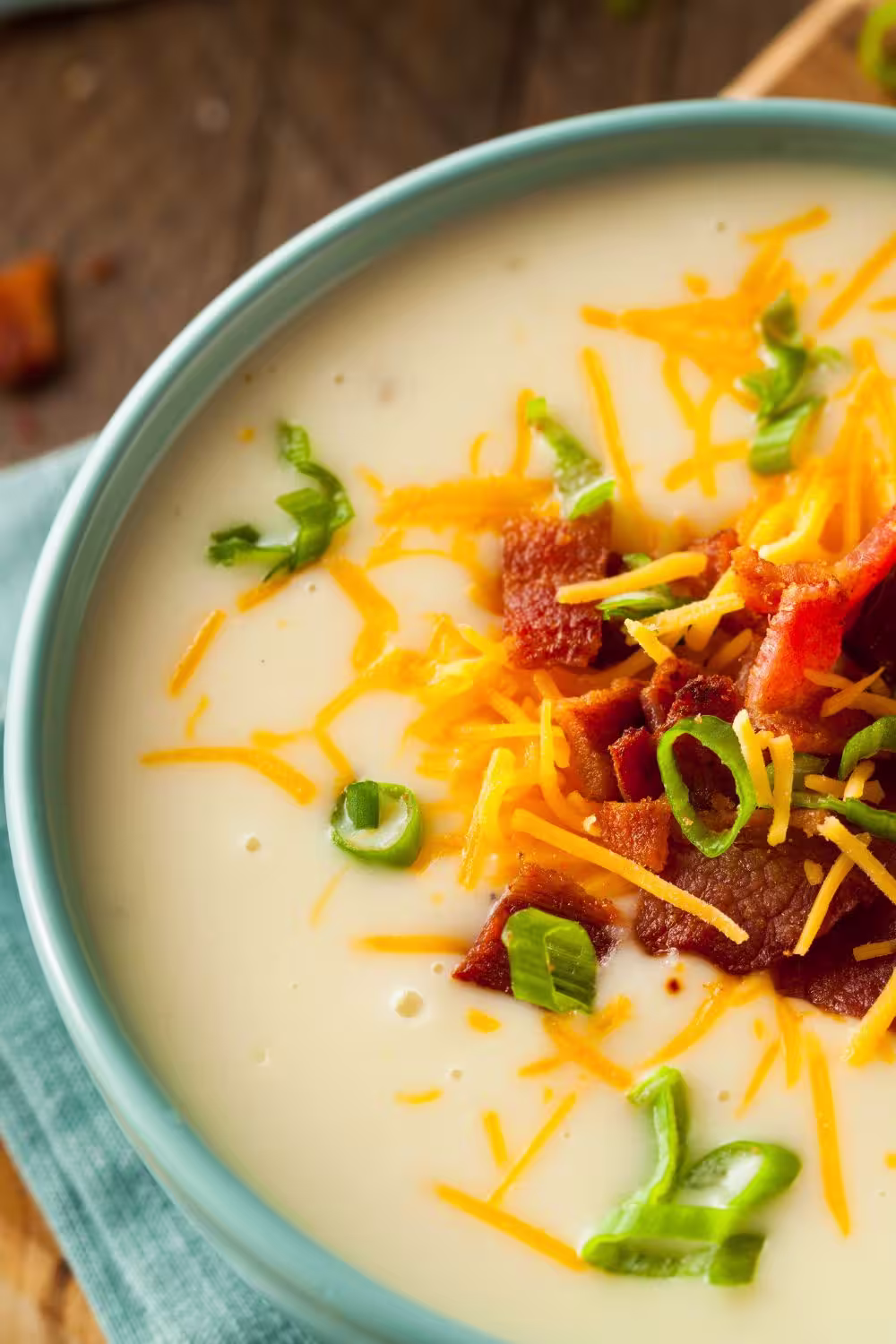 Close-up of creamy potato soup in a blue bowl with cheddar, bacon, and sliced green onions