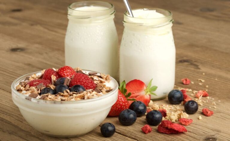 A bowl of homemade yogurt with fruit and granola in front of two mason jars of granola