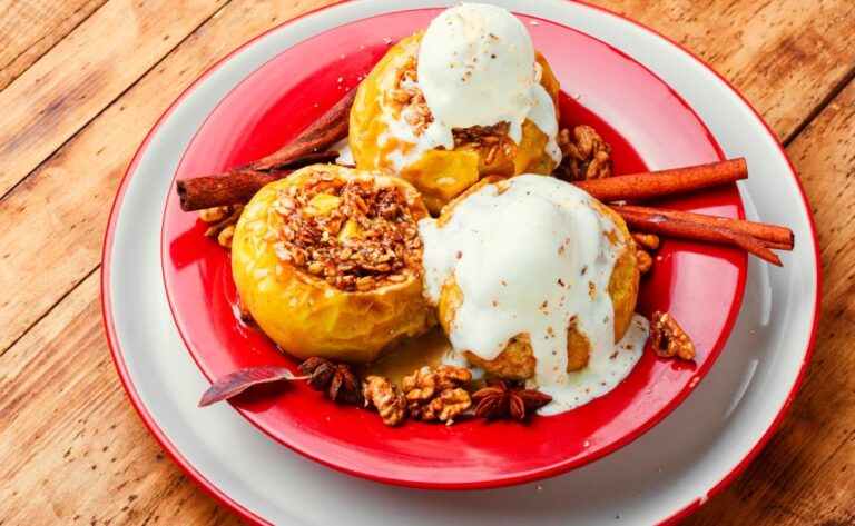 baked apples and ice cream on a red dish, displayed with cinnamon sticks, and nuts