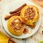 2 baked apples on a plate, displayed with cinnamon sticks